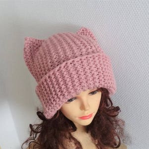 May include: A pink knitted beanie with cat ears. The beanie is made of a soft, textured yarn and has a simple, classic design.