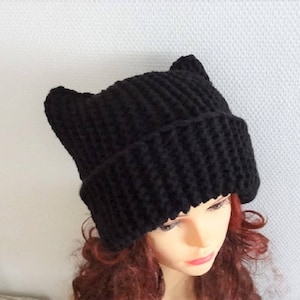 May include: Black knitted beanie with cat ears. The beanie is made of a soft, warm yarn and has a simple, classic design.