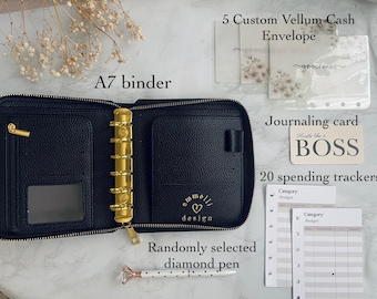 May include: A black A7 binder with gold fittings, a diamond pen, vellum cash envelopes, a journaling card with "Hustle like a BOSS", and spending trackers. The binder is open, showing interior pockets.