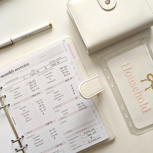 May include: A white planner with a monthly budget overview. The planner has sections for income, expenses, and savings. The planner is open to the page for the month of June. The planner has a white cover with a gold zipper. The planner is on a white surface. The text "*EXAMPLE ONLY*" is at the bottom of the page.