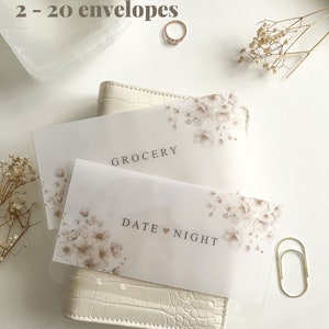 May include: Two floral-decorated envelopes labeled "Grocery" and "Date Night" rest on a white wallet. The text "Choose Your Quantity 2 - 20 envelopes" is at the top. A gold ring and paperclip are also visible.