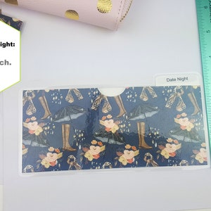 Puede incluir: Un sobre de cartera de pl&aacute;stico transparente con un patr&oacute;n azul y floral. El sobre tiene una solapa en la parte superior y mide aproximadamente 8,9 cm de alto. El texto "Date Night" est&aacute; escrito en el sobre.