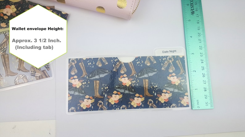 Puede incluir: Un sobre de cartera de pl&aacute;stico transparente con un patr&oacute;n azul y floral. El sobre tiene una solapa en la parte superior y mide aproximadamente 8,9 cm de alto. El texto "Date Night" est&aacute; escrito en el sobre.