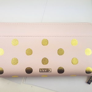 Puede incluir: Una cartera de cuero rosa con lunares dorados y el texto "kikki.k" en la parte delantera. La cartera mide aproximadamente 10 cm de alto.