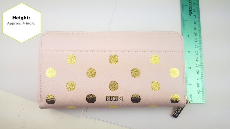 Puede incluir: Una cartera de cuero rosa con lunares dorados y el texto "kikki.k" en la parte delantera. La cartera mide aproximadamente 10 cm de alto.