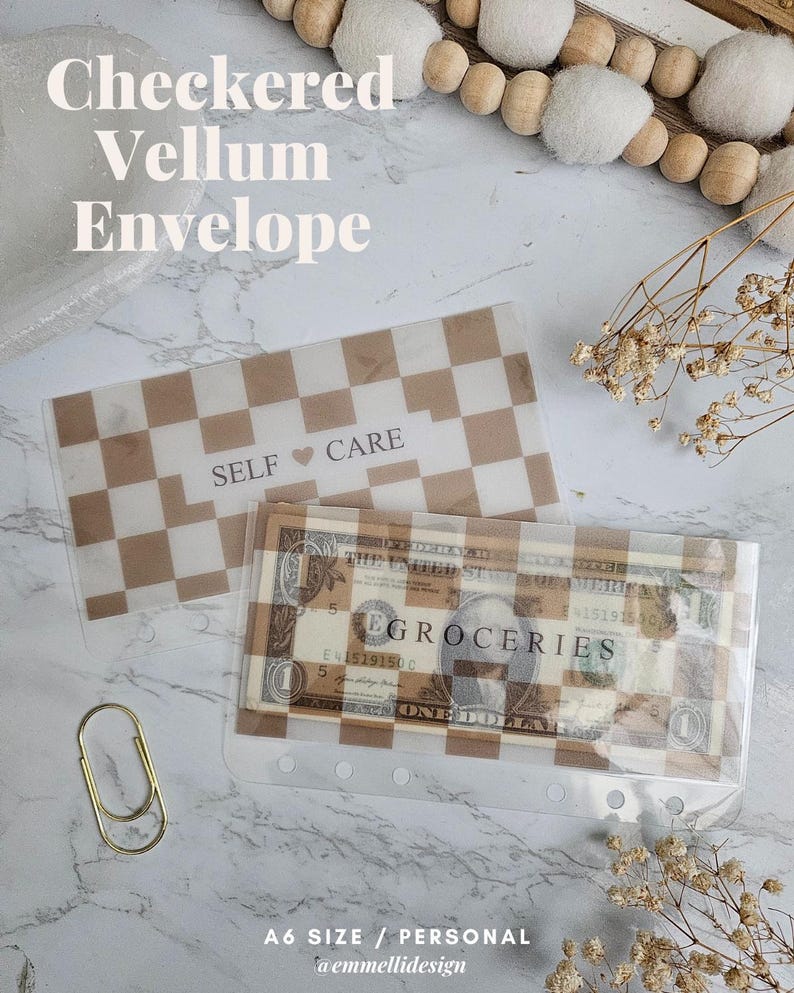 K&ouml;nnte beinhalten: Zwei transparente Vellum-Umschl&auml;ge mit einem braun-wei&szlig;en Schachbrettmuster. Einer hat die Aufschrift "SELF CARE". Der andere enth&auml;lt einen Geldschein und das Wort "GROCERIES". Links ist eine goldene B&uuml;roklammer.