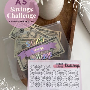May include: A pink and white printable A5 savings challenge chart with a $1000 savings goal. The chart has a grid of circles with different dollar amounts in each circle. The chart is on a table with a clear plastic bag containing US dollar bills.