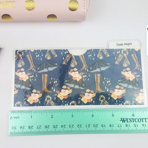 Puede incluir: Un sobre de cartera de pl&aacute;stico transparente con un patr&oacute;n azul y floral. El sobre mide 17 cm de largo. El texto "Date Night" es visible en el sobre.