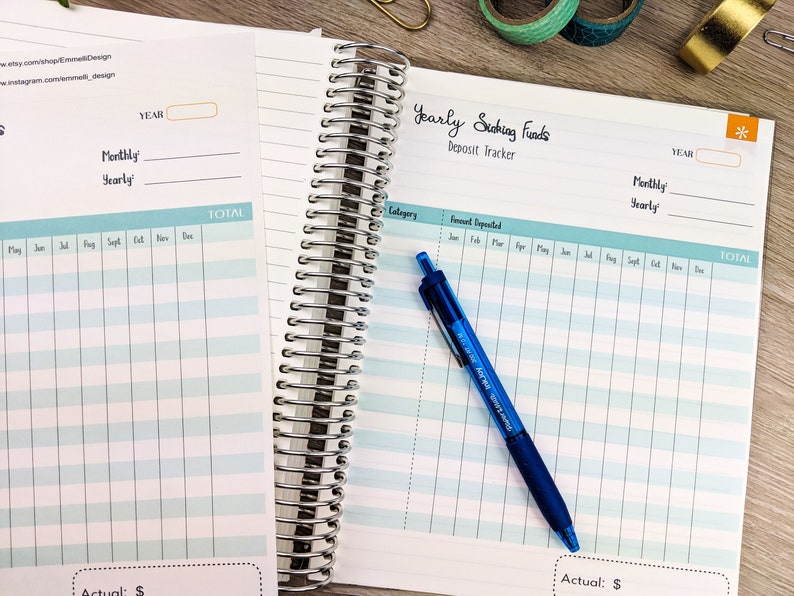 May include: A close-up of a blue spiral bound notebook with a light blue and white gridded page. The page is labeled "Yearly Saving Funds Deposit Tracker" and has columns for category, amount deposited, and months of the year. A blue pen is lying on the page.