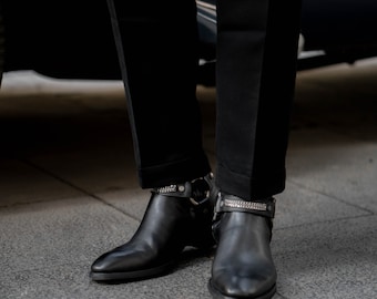May include: Black leather ankle boots with silver chain accents. The boots have a pointed toe and a low heel.