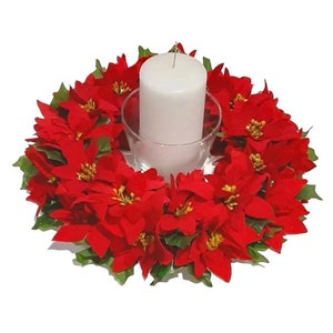 May include: A festive Christmas centerpiece featuring a white pillar candle in a clear glass holder, surrounded by a wreath of vibrant red poinsettia flowers with green leaves. The arrangement is perfect for holiday decor.