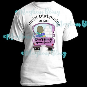 May include: White t-shirt with a pink truck design. The truck is carrying toilet paper and hand sanitizer. The text "Social Distancing 2020" is above the truck and "Don't touch your face!" is below the truck.