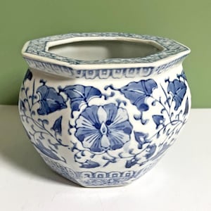 May include: An octagonal ceramic planter featuring a white base with blue floral and vine patterns. The rim and base are decorated with intricate geometric borders, while the body displays large, stylised blossoms and leafy vines.