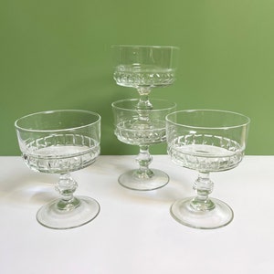May include: Four clear glass champagne coupes with a cut glass design. The coupes are stacked on top of each other.