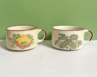 May include: Two cream-colored ceramic soup mugs with brown rims and handles. One mug features a yellow chicken design, the other has a green celery design. Both mugs are decorated with colorful illustrations.