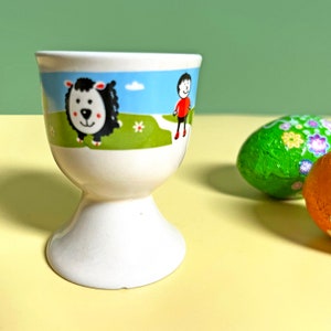 Vintage egg cup with retro illustrations of countryside farm with black sheep, boy, farmer etc children's novelty egg cup