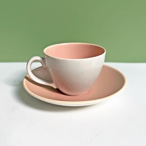 Op de afbeelding: Een roze theekopje en schotelset. Het kopje heeft een witte binnenkant en een roze buitenkant. De schotel is effen roze.