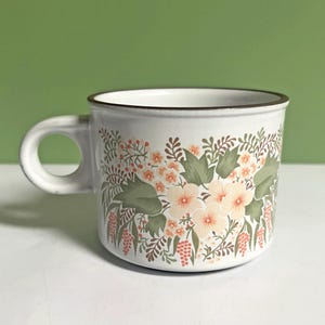 May include: White ceramic mug with a floral design. The mug has a brown rim and handle, and is decorated with a pattern of flowers, leaves, and berries in peach, green, and brown. Suitable for hot drinks, it's a classic kitchenware item.