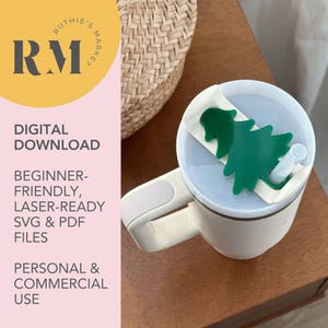 May include: White ceramic travel mug with a lid featuring a green Christmas tree design. The mug has a handle and a straw.