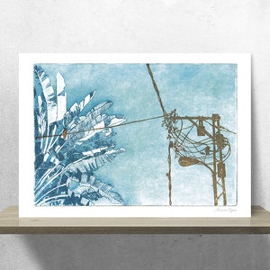 May include: A blue and white print of a palm tree with a tangle of power lines and a streetlight in the background. The print is signed "Laura Yglesias".