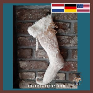 Puede incluir: Una media de Navidad blanca de ganchillo con un diseño de encaje y un puño blanco esponjoso. La media tiene forma de bota y tiene una punta puntiaguda. La media está colgada en una pared de ladrillo.