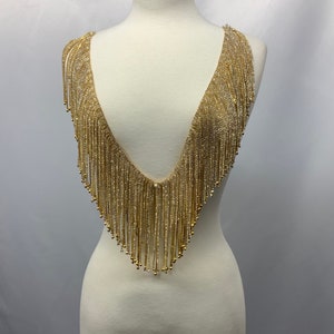 May include: Gold beaded fringe trim with a V-neck shape. The fringe is made of small, round beads that are strung together to create a cascading effect.