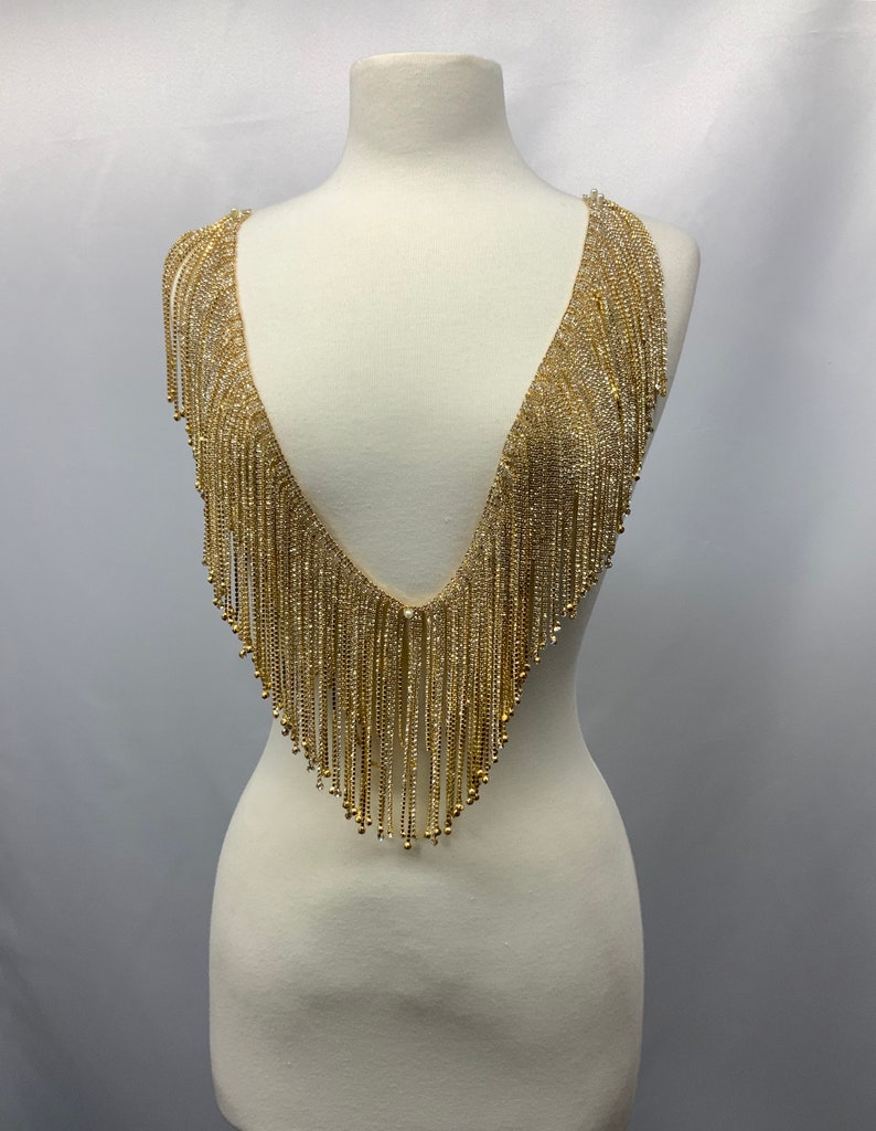 May include: Gold beaded fringe trim with a V-neck shape. The fringe is made of small, round beads that are strung together to create a cascading effect.