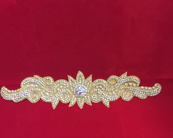 May include: A gold and crystal embellishment with a floral design. The embellishment is on a red background.