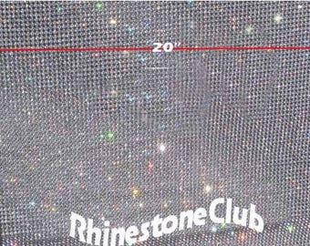 Pode incluir: Uma folha de tecido de strass transparente e brilhante que mede 50,8 cm por 121,9 cm. O tecido é feito de pequenos strass redondos que estão muito próximos. O tecido é etiquetado como "Rhinestone Club".