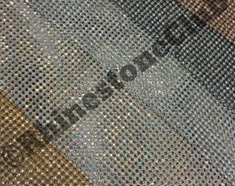 May include: A close-up of a sheet of iridescent rhinestones, with rows of gold, silver, and black rhinestones. The rhinestones are arranged in a grid pattern.
