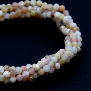 May include: A strand of pink, white, and yellow gemstone beads. The beads are faceted and have a slightly irregular shape.