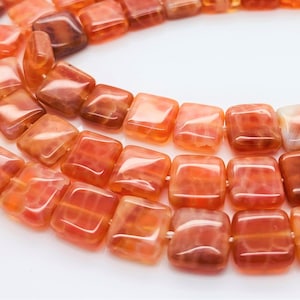 May include: A strand of orange agate square beads. The beads are translucent and have a marbled pattern.