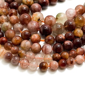 May include: Strands of gemstone beads in various shades of brown, red, and clear. The beads are round and appear to be made of a translucent material. The beads are strung on orange thread, and are suitable for jewelry making.