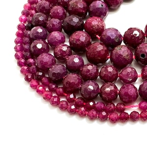 May include: Close-up of multiple strands of faceted, deep red gemstone beads. The beads, in various sizes, have a textured surface and are strung together. The deep red beads create a layered effect. The beads are a deep, saturated red colour.