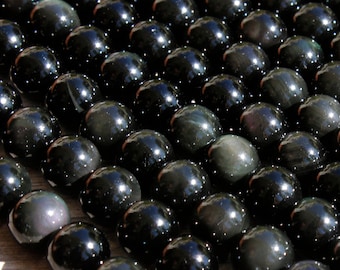 May include: A strand of black obsidian beads with iridescent rainbow flashes. The beads are round and smooth, and they are arranged in a row. The beads are illuminated by sunlight, which highlights their iridescent qualities.