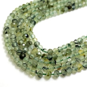 May include: A strand of green gemstone beads. The beads are round and have a faceted finish. The beads are strung on a clear thread.