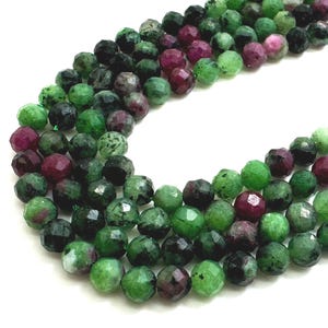 May include: Strands of faceted gemstone beads in shades of green and burgundy. The beads are round and have a polished, reflective surface. The gemstones are strung together, creating a necklace or bracelet.