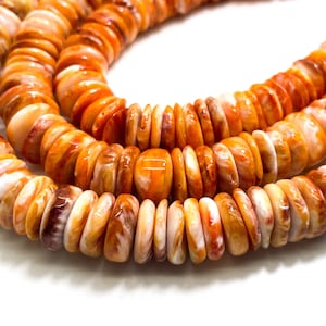 以下が含まれることがあります： オレンジと白の貝殻ビーズの連なり。平らな円盤状のビーズが連なっており、ネックレスやブレスレットになっています。色は薄いクリーム色から濃いオレンジ色まであり、貝殻の自然な風合いが特徴です。