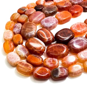 May include: A collection of polished, oval-shaped beads in shades of orange, red, and brown. The beads have a marbled appearance and are strung together, likely for jewelry making. The background is white.