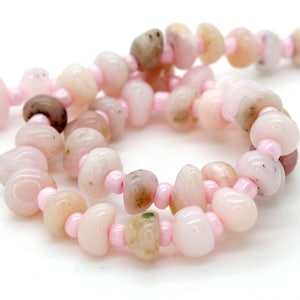 May include: A strand of pink and white gemstone beads with a smooth, pebble-like shape. The beads are strung on a thin pink thread.