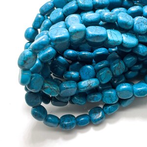 Puede incluir: Una hebra de cuentas de piedra turquesa azul, cada cuenta es de forma cuadrada lisa con bordes redondeados.