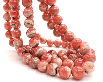 May include: A strand of round, polished beads in shades of coral, salmon, and peach. Each bead features unique, swirling patterns of white and dark gray mineral inclusions, creating a marbled effect throughout the smooth, spherical surface.