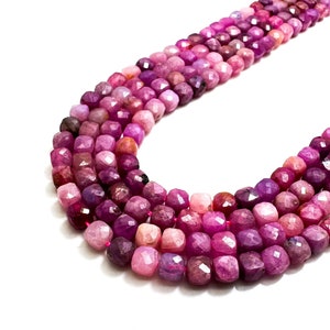 Może przedstawiać: Szereg różowych i fioletowych koralików z kamieni szlachetnych. Koraliki są fasetowane i mają kwadratowy kształt. Koraliki są nawleczone na przezroczystą nić.