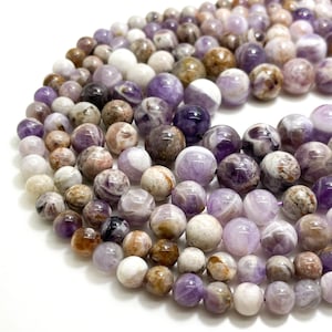May include: A strand of round, purple, white, and brown amethyst beads. The beads are smooth and have a natural, polished finish. The beads are arranged in a circular pattern, with the largest beads in the center and the smallest beads on the outside.