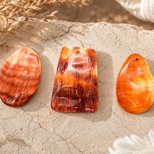 May include: Four flat, polished shell pendants in varying shapes and shades of orange, red, and cream. Each piece features a smooth, glossy surface with natural striations and a small drilled hole at the top for hanging as jewelry components.