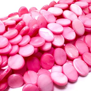 May include: A pile of pink, oval-shaped beads. The beads vary in shade from light to deep pink, with a glossy finish. The beads are strung together, suggesting they are for jewelry making or crafting.