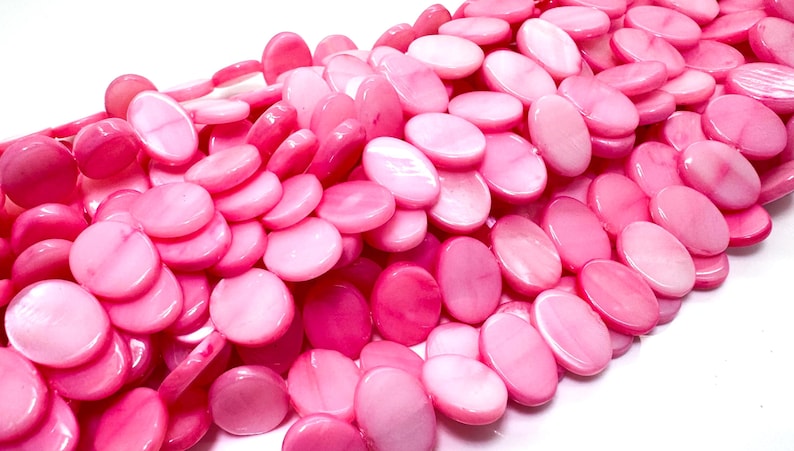 May include: A pile of pink, oval-shaped beads. The beads vary in shade from light to deep pink, with a glossy finish. The beads are strung together, suggesting they are for jewelry making or crafting.