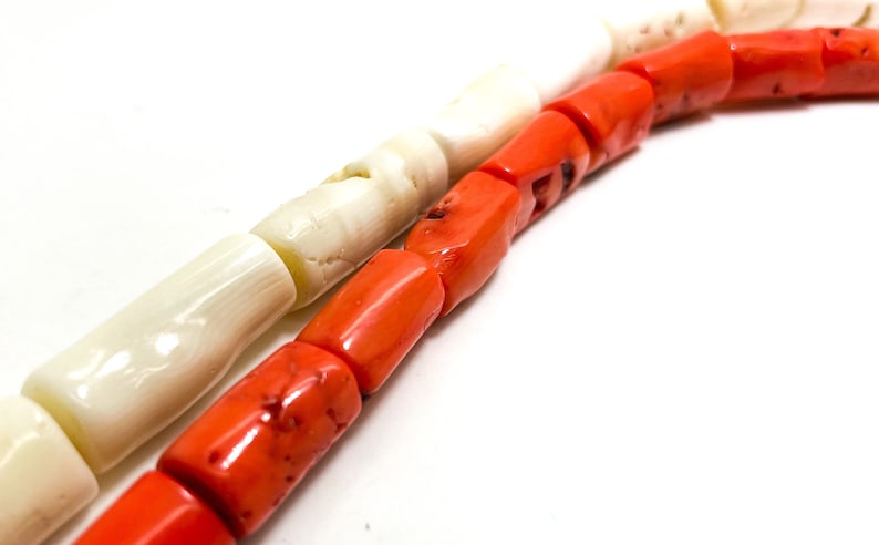 May include: A strand of white and orange beads. The beads are cylindrical and have a smooth, polished finish. The white beads are made of shell and the orange beads are made of coral.