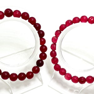 May include: Two red gemstone bracelets with round beads. The bracelets are on display on clear stands.