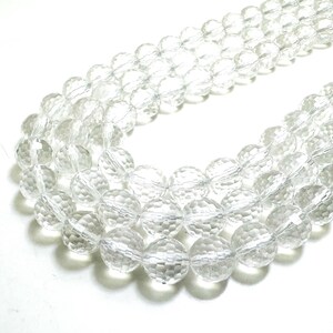 May include: Clear, faceted crystal beads strung together, forming multiple strands. The beads are round with a textured surface, reflecting light. The image shows a close-up of the beads, highlighting their transparency and intricate design. These beads are suitable for jewelry making.